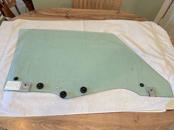The new door glass ready for installation.  The three circular fasteners have 1/4" studs that mount it to the regulator and there is a bit of play in the placement of these studs. I used an extra regulator to align the studs before tightening them to the new glass.