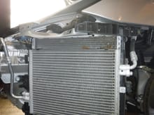 View of left condenser with radiator behind it. 
 The electric fan is behind the radiator.  Note the road debris that collects.  These assemblies need to be cleaned. 