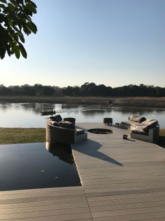 View from camp of boat approaching; safari vehicles line up on far side for guests