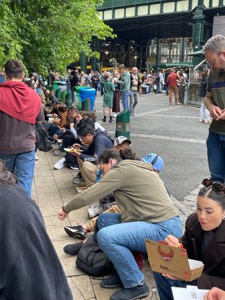 People sitting on the curb at Borough Market.  Any flat place is game for a dinner table.