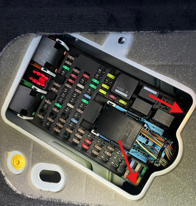 The 10mm nuts holding the fuse panel are indicated by arrows. But the panel will not move to the right enough to release the indicated cover.