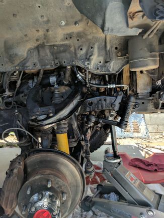 Jack with a bar that is pushing against steering pump to keep it nice and tight.